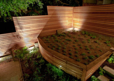 Urban Mood Lighting: Small city garden comes alive at night with light-washed redwood fences and curved retaining walls lit from within.