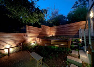 Urban Mood Lighting: Small city garden comes alive at night with light-washed redwood fences and curved retaining walls lit from within.